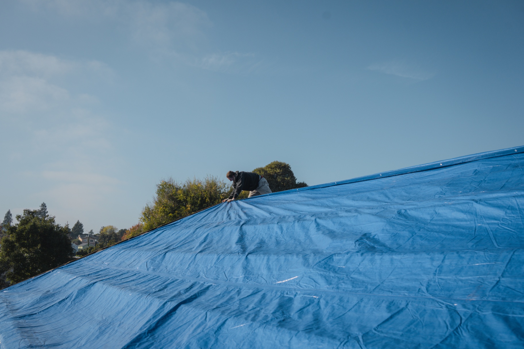 Worker securing a blue tarp over a roof for weather protection