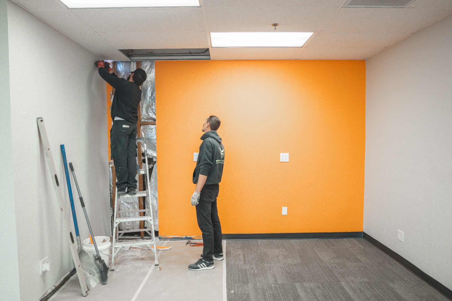 Crew finishing trim around freshly painted orange accent wall