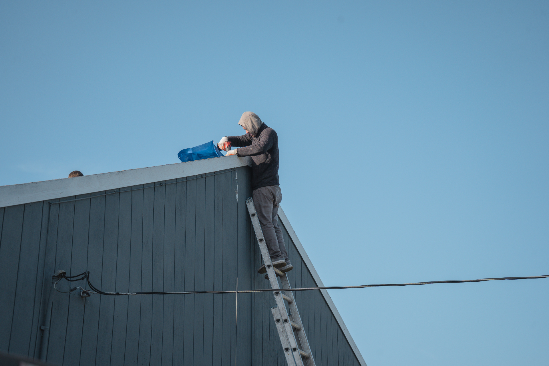 Roofer on ladder working at the peak of a gray building