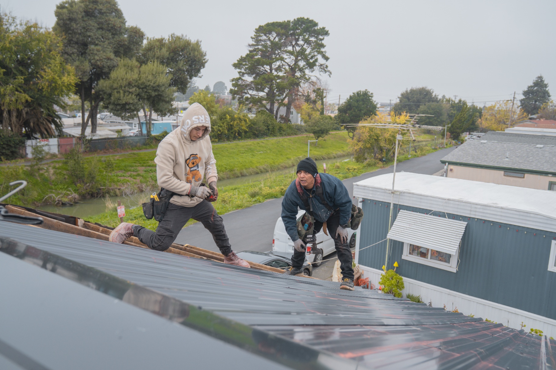 Two roofers installing new metal roofing panels on a home